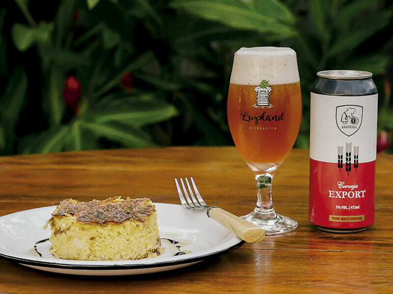 Prato com sopa paraguaia ao lado de copo e lata de cerveja