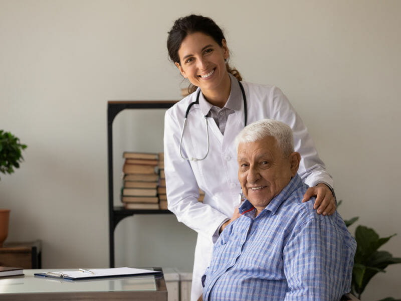 Idoso sentado em consultório médico e médica em pé atrás dele