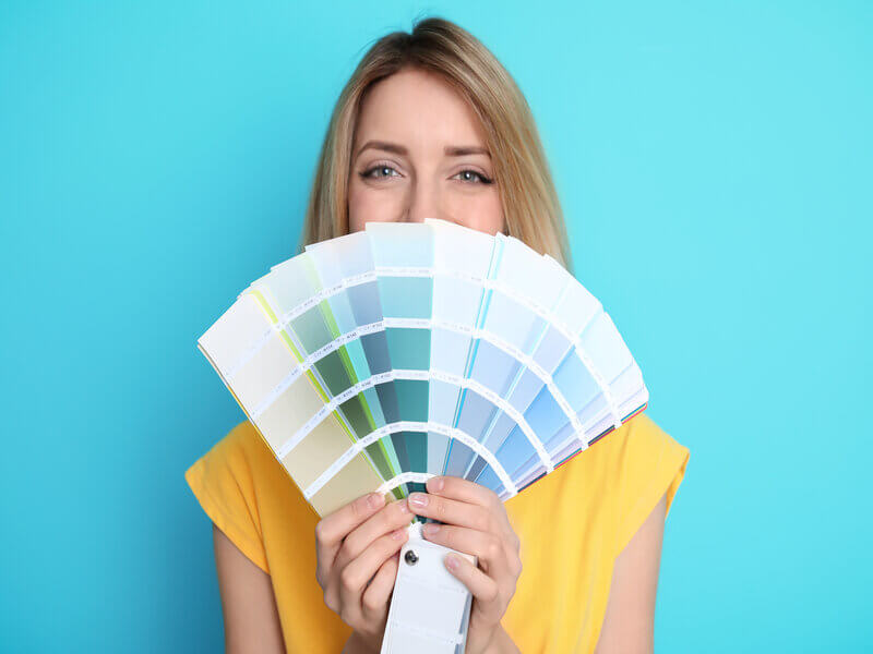 Mulher de blusa amarela segurando paleta de cores em frente a um fundo azul
