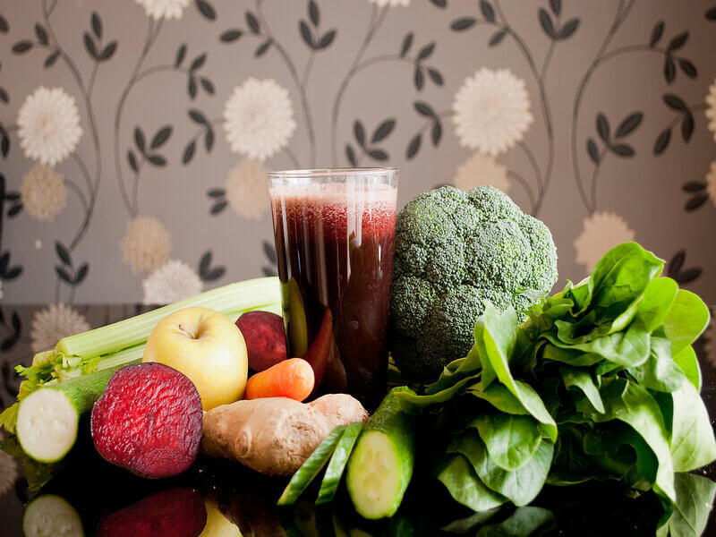 Copo com suco roxo com maçã, beterraba, gengibre e cenoura ao redor