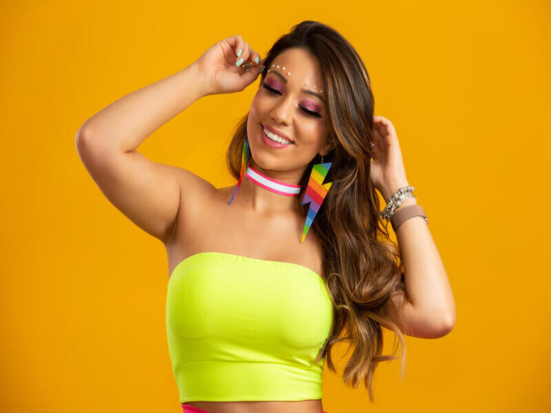 Mulher sorrindo com as mãos no cabelo em frente a um fundo amarelo