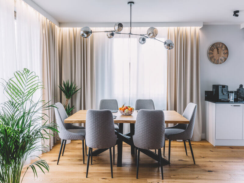 Sala de jantar com cadeiras cinzas, mesa e cortinas de fundo