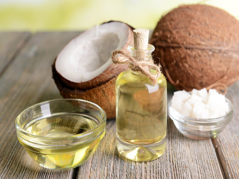 Recipientes de vidro com óleo e pedaços de coco ao fundo em cima de uma mesa de madeira