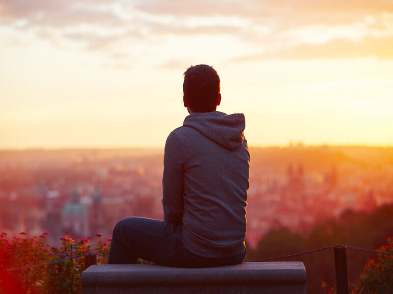 Homem sentado olhando o por do sol
