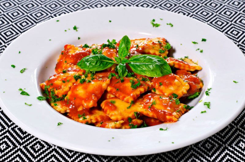 Ravióli com molho de tomate e manjericão em prato branco