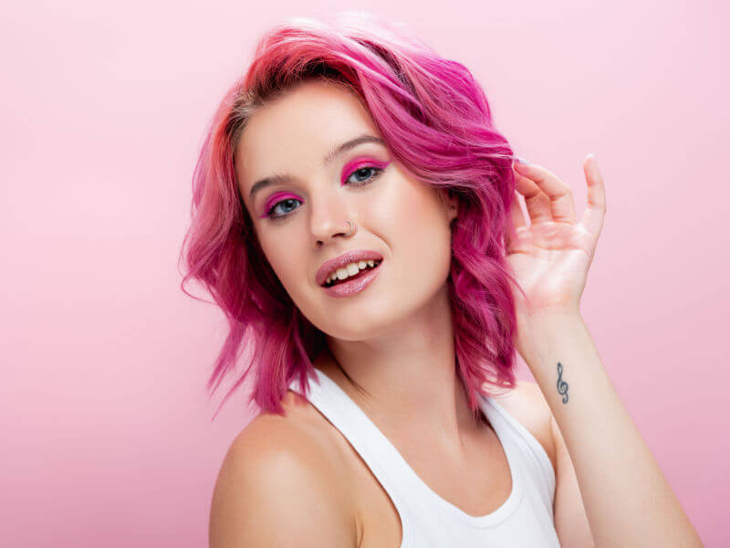 Mulher com cabelo rosa em frente a um fundo rosa
