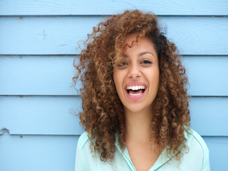 Mulher de cabelo cacheado sorrindo em frente a um fundo azul