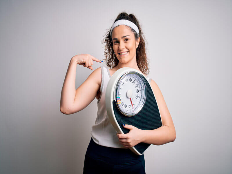 Mulher sorrindo com roupa de academia segurando uma balança