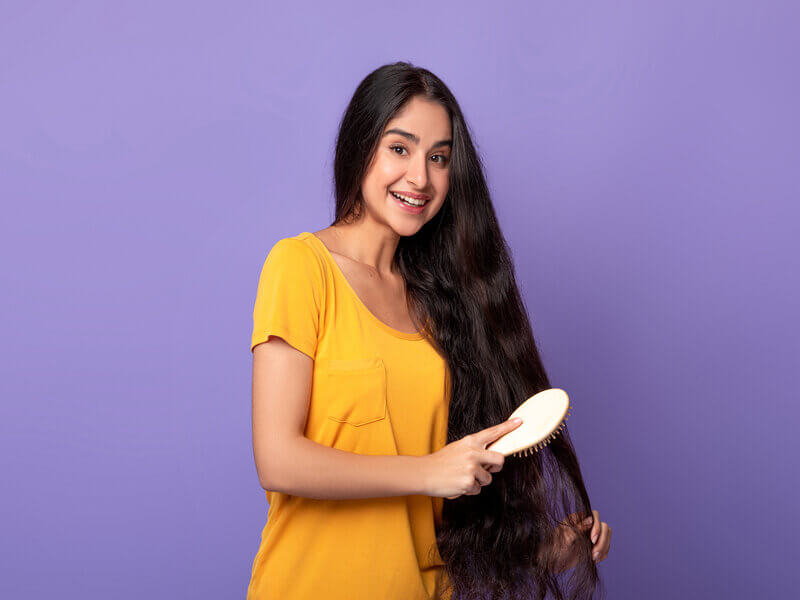 Mulher de blusa amarela penteando cabelo em frente a um fundo roxo