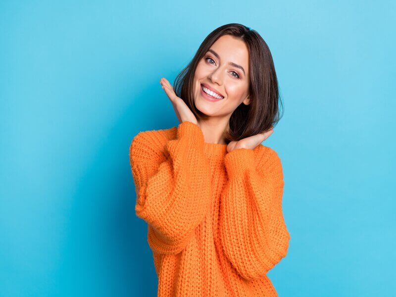 Mulher de blusa laranja com as mãos na cabeça sorrindo