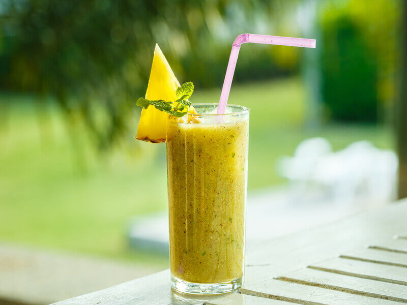 Copo de vidro com suco amarelo decorado com uma fatia de abacaxi e folhas de hortelã