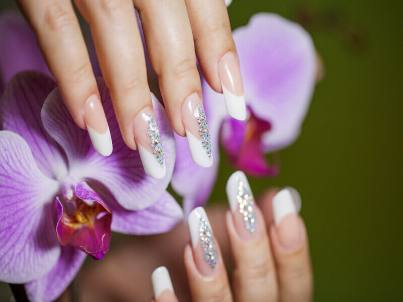 Unhas pintadas de branco em cima de uma orquídea