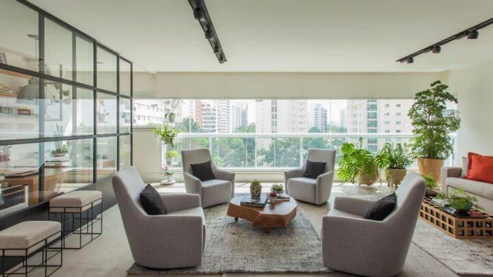 uma sala de estar bastante arejada com quatro poltronas e vidro na sacada e interior da casa