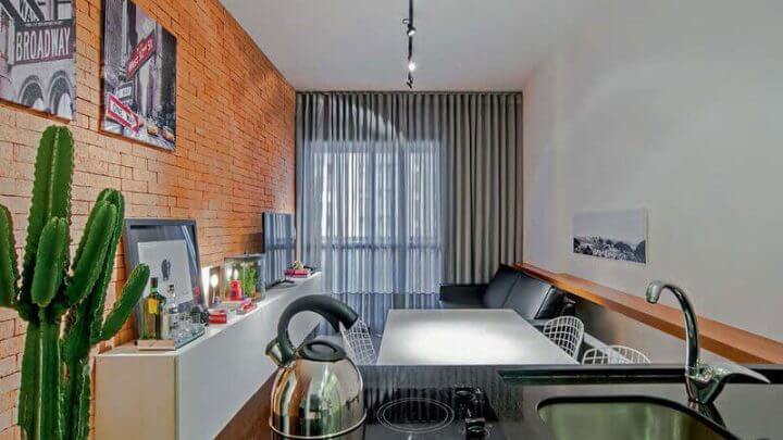 Sala de estar com parede laranja e sofá preto integrada com cozinha