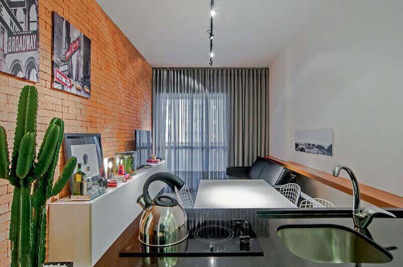 Sala de estar com parede laranja e sofá preto integrada com cozinha