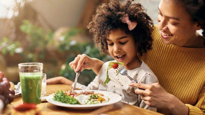 Mulher dando comida saudável para filha pequena.