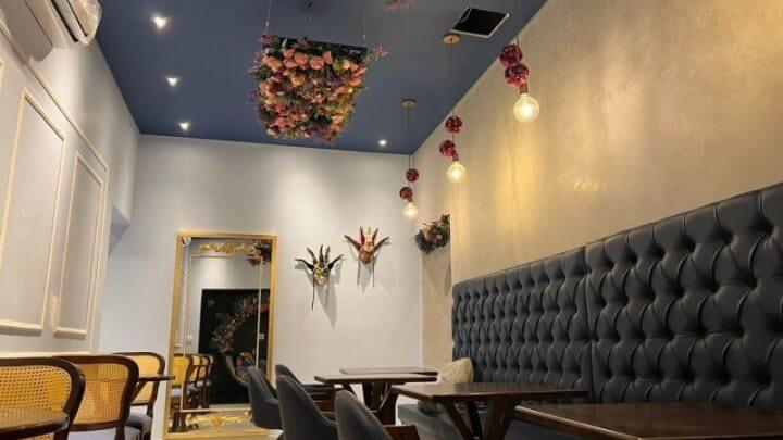 Ambiente decorado com cadeiras e estofado escuro, paredes cinza e flores no teto