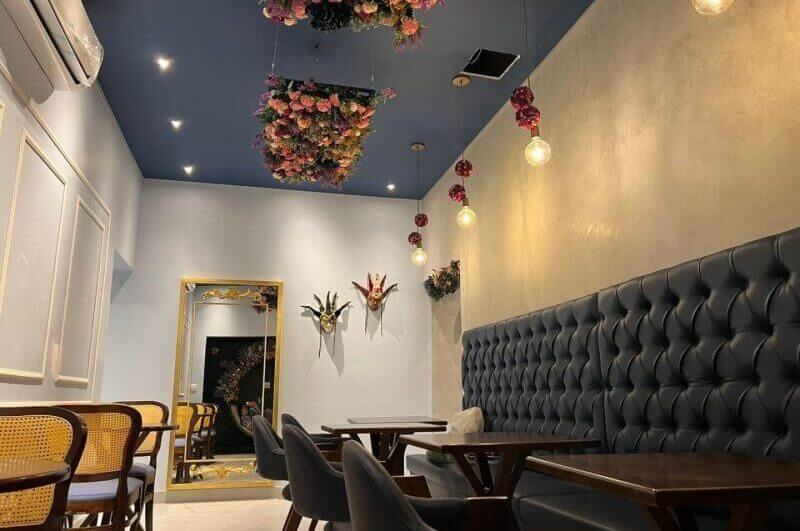 Ambiente decorado com cadeiras e estofado escuro, paredes cinza e flores no teto