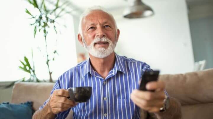 Senhor assistindo televisão e segurando xícara de café