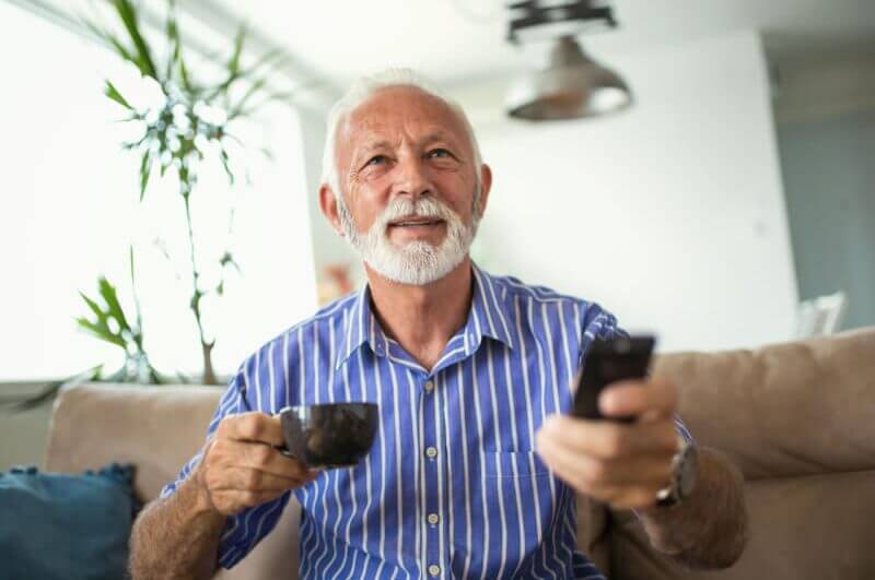 Senhor assistindo televisão e segurando xícara de café