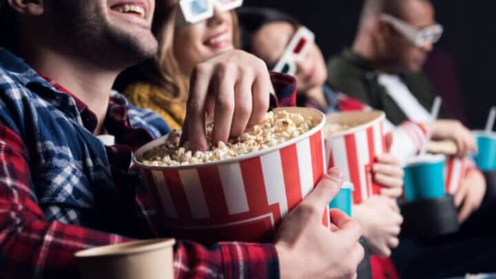 Jovens amigos sorridentes em óculos 3d comendo pipoca e assistindo filme no cinema