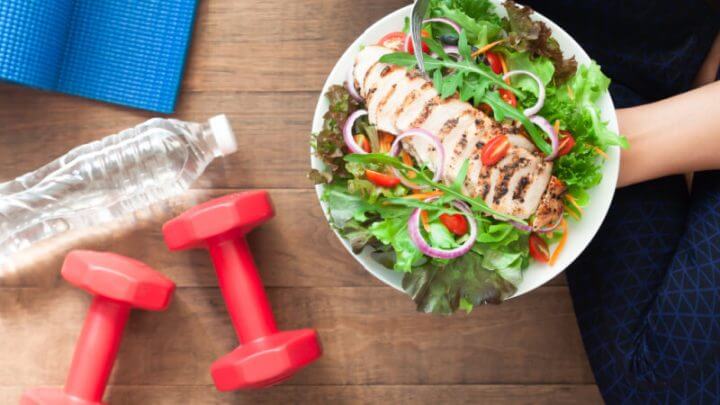 Comida saudável e fitness. Prato de salada de frango com equipamentos de ginástica