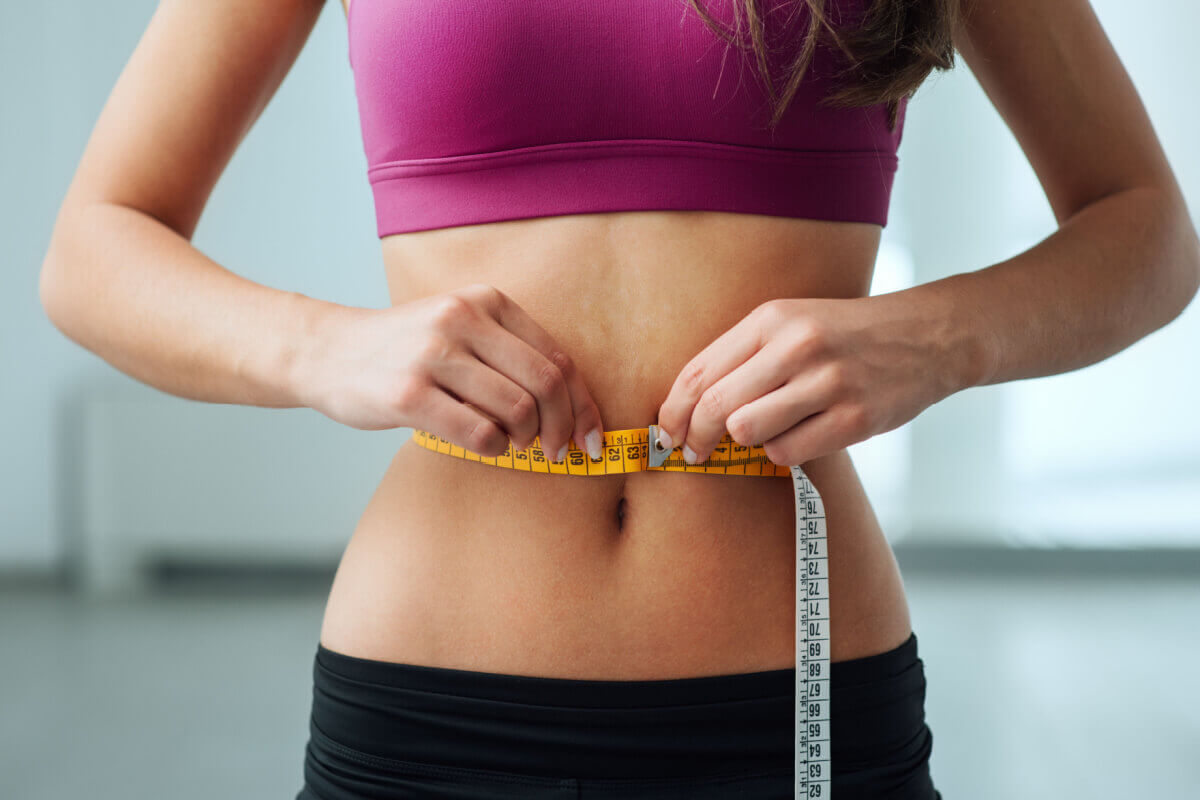 Mulher magra medindo sua cintura com fita métrica