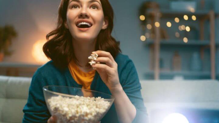Jovem mulher assistindo projetor, TV, filmes com pipoca à noite. Garota passando um tempo em casa.