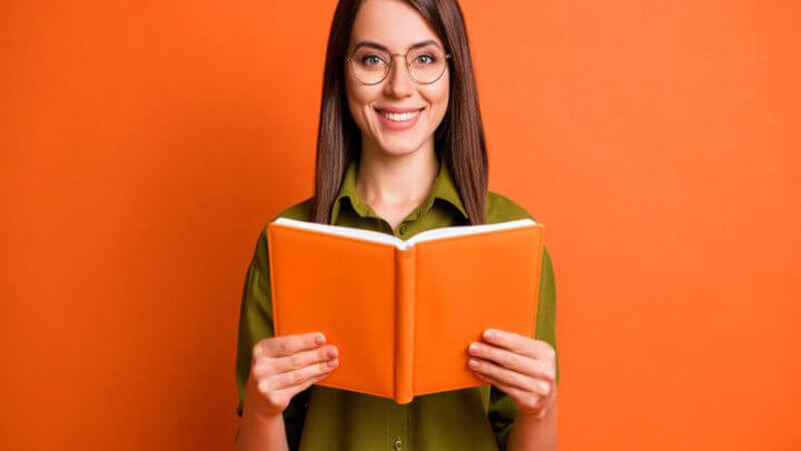 Mulher de blusa verde sorrindo segurando um livro