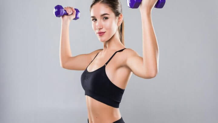 Mulher com roupa de academia preta levando peso