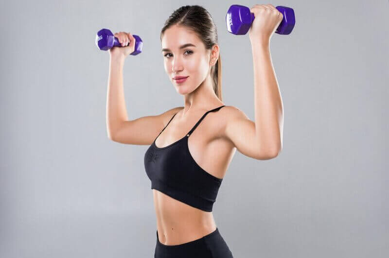 Mulher com roupa de academia preta levando peso