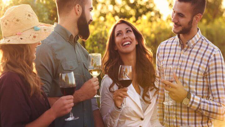 Pessoas sorrindo segurando taças com vinho em um parque