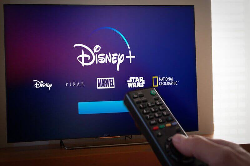 Logo do Disney+ em uma televisão com pessoa segurando um controle remoto