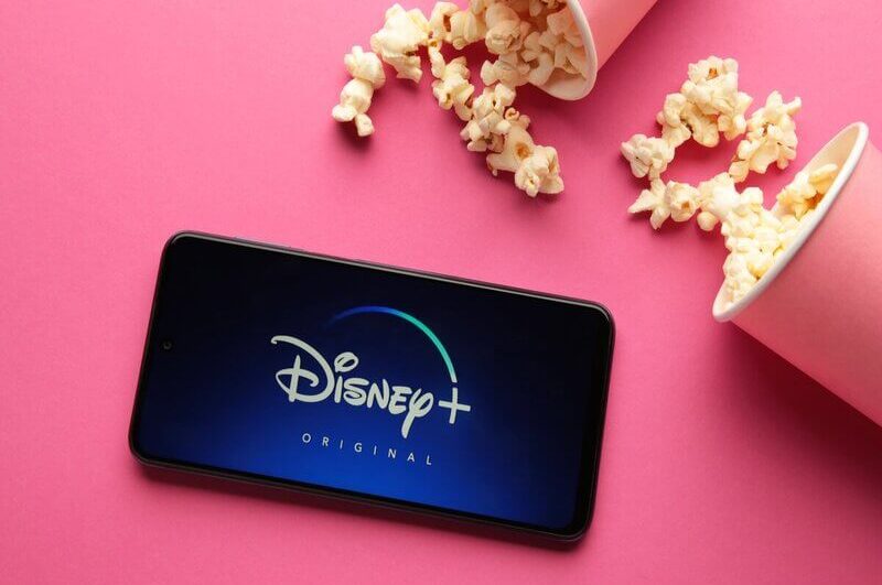 Logo do Disney Plus e um celular com copos de pipoca rosa ao lado