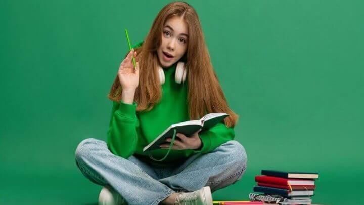 Menina de blusa verde sentada olhando um livro