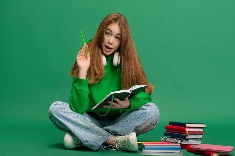 Menina de blusa verde sentada olhando um livro