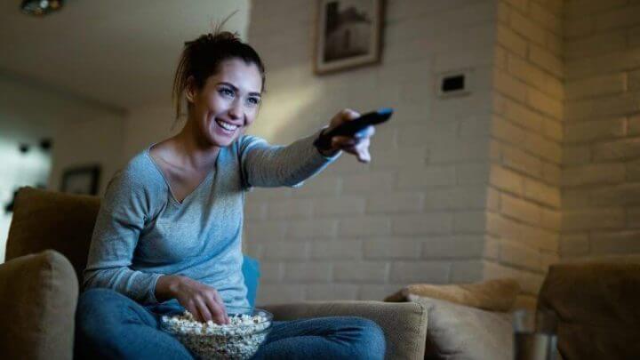 Mulher apontando controle para televisão enquanto come pipoca