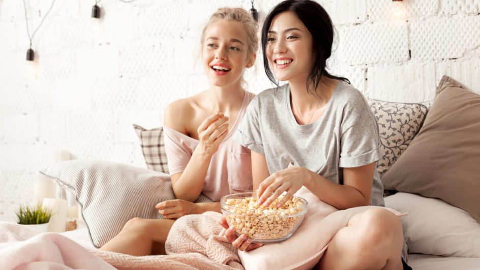 Amigas alegres comendo pipoca e assistindo filme com alegria. Atmosfera acolhedora e amigável
