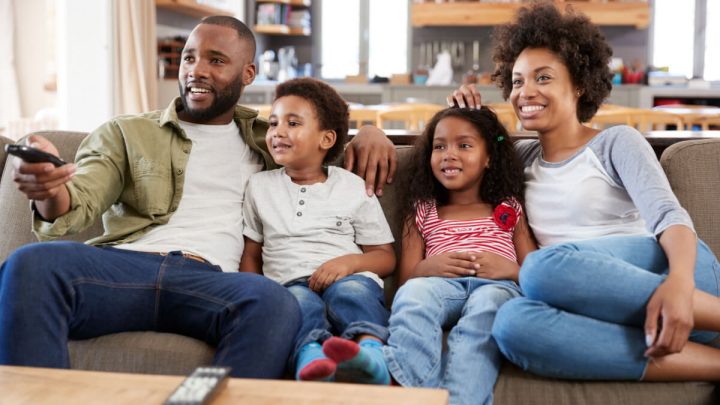 Família sentada no sofá da sala assistindo à televisão