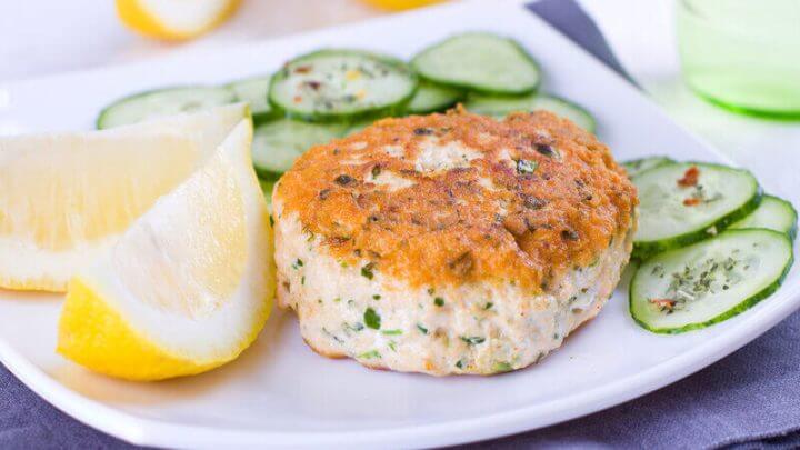 Prato branco com hambúrguer de salmão, rodelas de pepino e limão