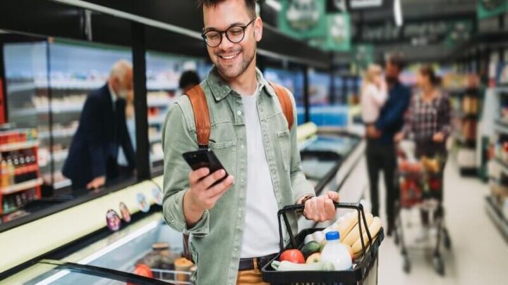 Homem sorrindo mexendo no celular em um supermercado