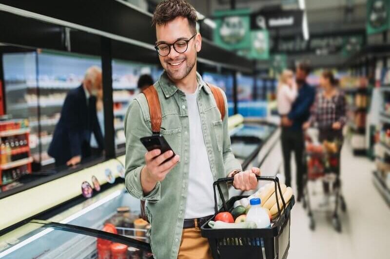 Homem sorrindo mexendo no celular em um supermercado