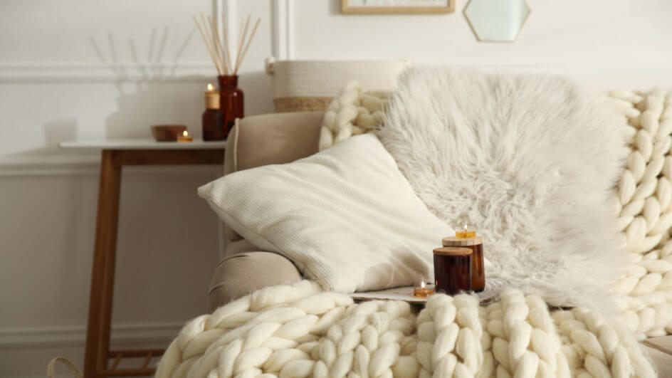 Velas no sofá bege com cobertor de malha. Design de interiores