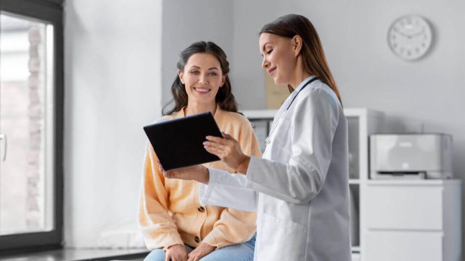 Médica com prancheta na mão atendendo a uma outra pessoa do sexo feminino