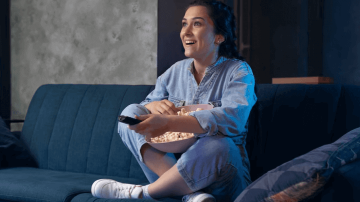 Mulher sentada em sofá com balde de pipoca assistindo a filme