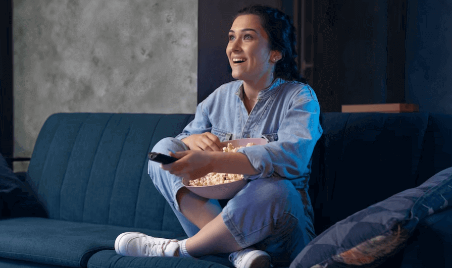 Mulher sentada em sofá com balde de pipoca assistindo a filme