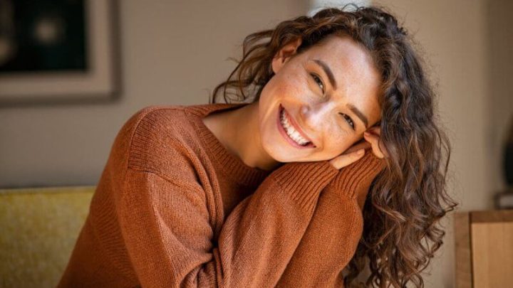 Mulher jovem feliz sentada no sofá em casa e olhando para a câmera