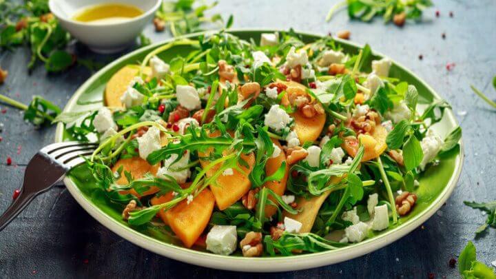 Salada com folhas de rúcula, caqui, queijo feta e nozes em um prato grande