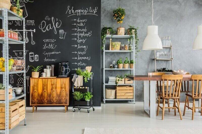 Sala com lousa na parede, móveis de madeira e estante com plantas