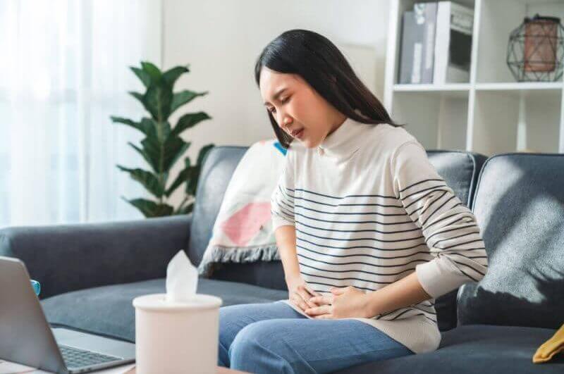 Mulher com as mãos na barriga demonstrando que está com dor